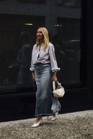 woman in a maxi denim skirt, striped button down shirt top, white heels, white bag