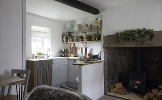 A small kitchen with white cabinets, distressed wood open shelving and wood countertops in a country style with original beamsby Ikea