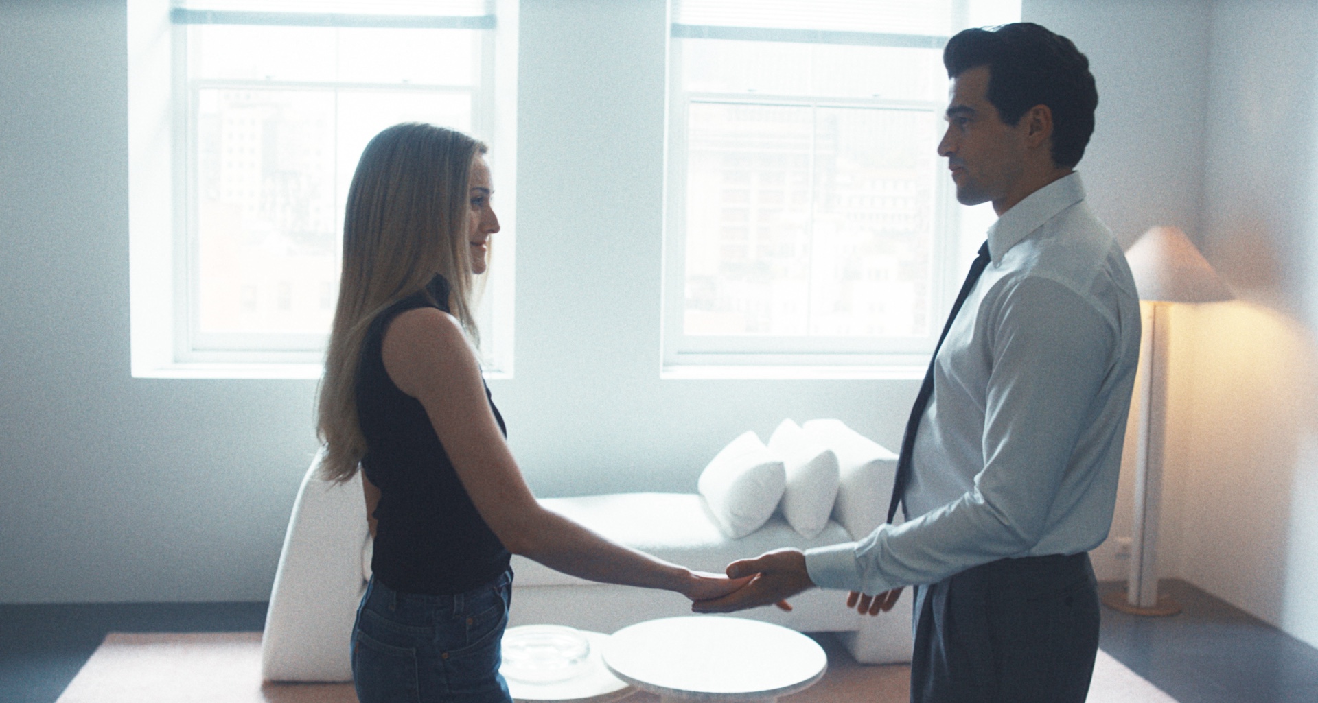 Sarah Pidgeon as Carolyn Bessette smiling and holding Paul Anthony Kennedy as John F. Kennedy Jr's hand in their apartment in FX's Love Story: John F. Kennedy Jr. &amp;amp; Carolyn Bessette episode &amp;quot;Exit Strategy&amp;quot;