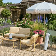 A blooming garden with a yellow striped outdoor lounge set, a green striped parasol with a fringed trim set next to the set