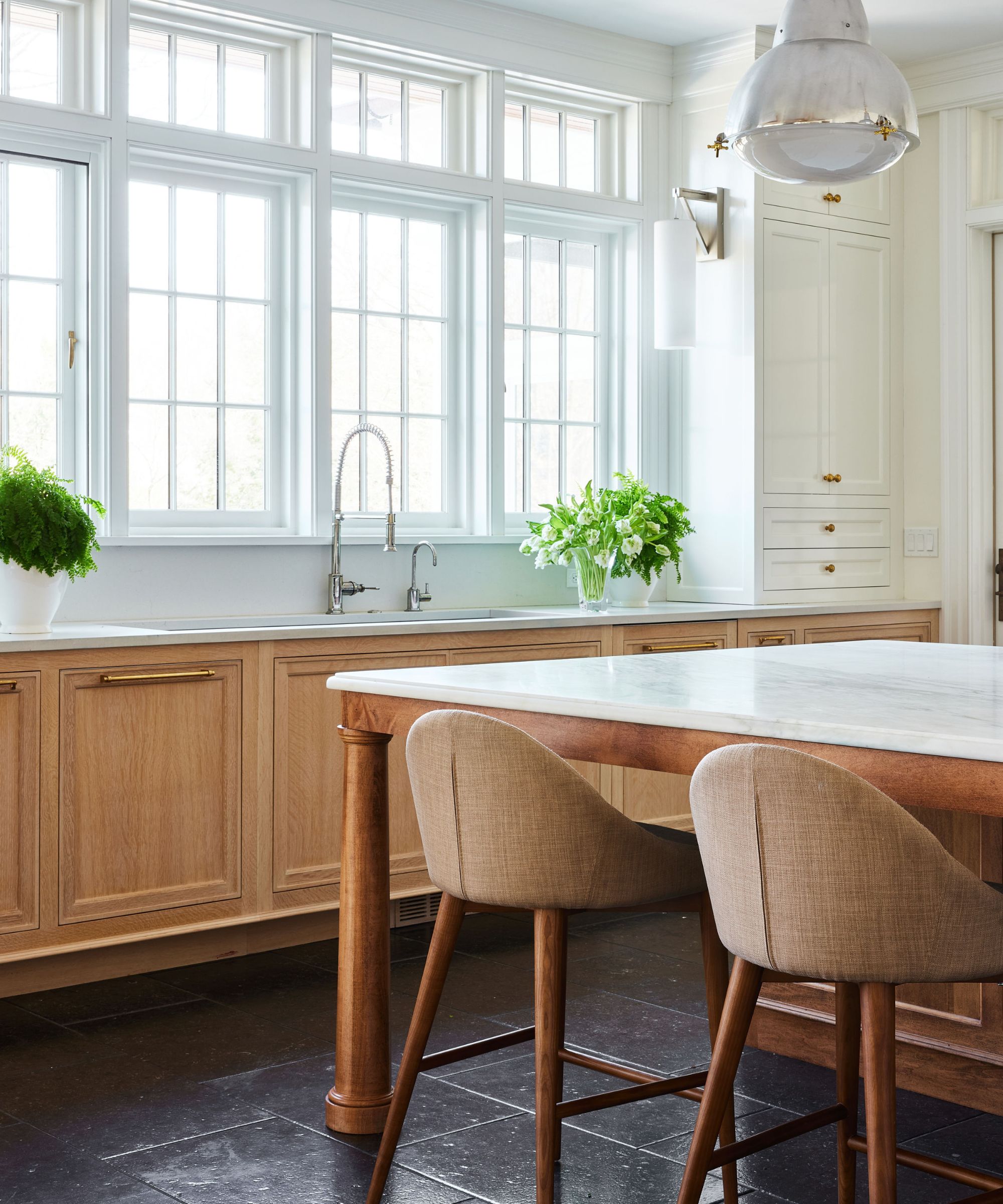 traditional kitchen with large windows, wooden cabinets, and white upper cabinets with an island and bar stools
