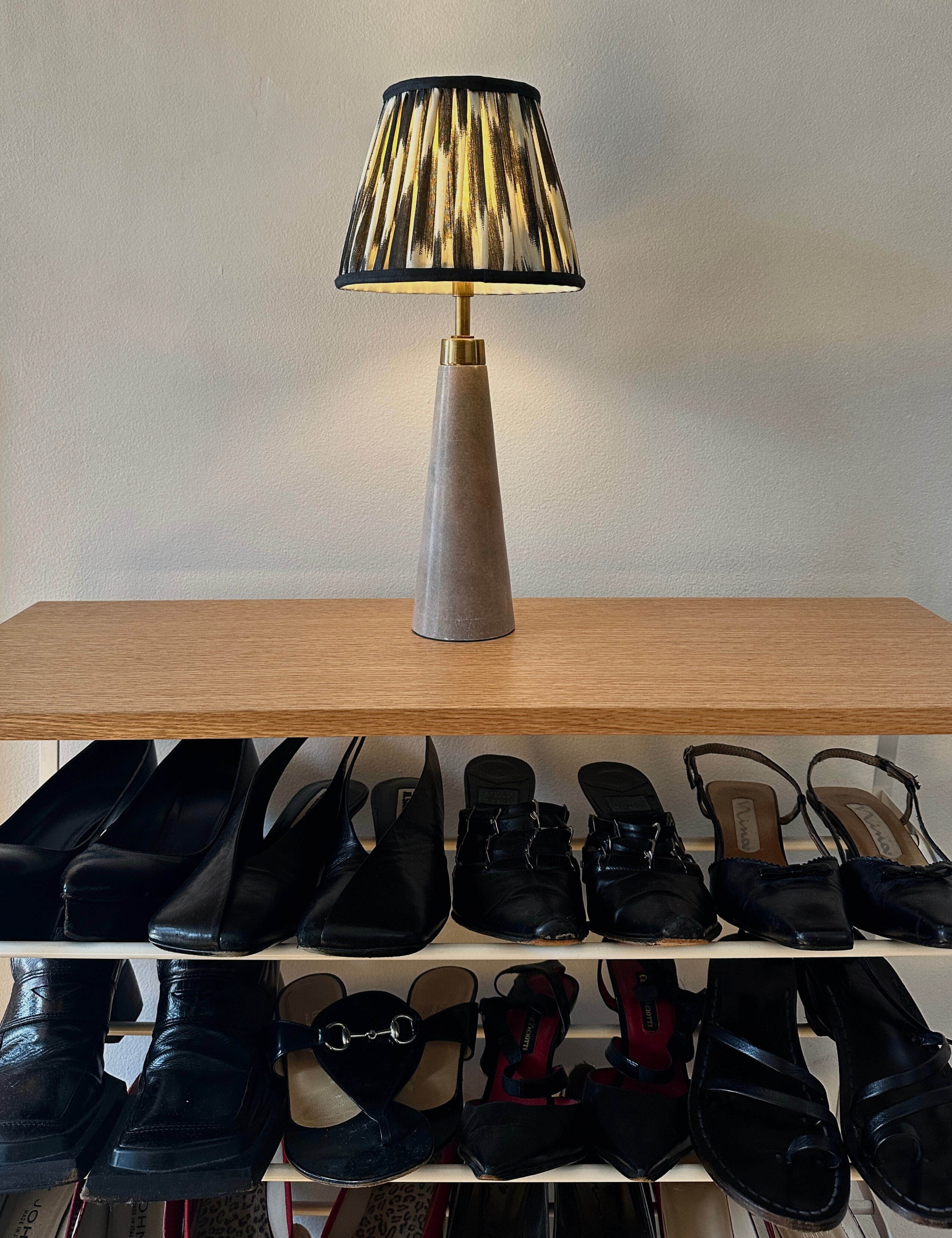 Ikat shaded table lamp resting atop of a wooden shoe rack