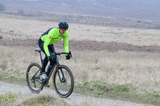 man riding a black gravel bike wearing a yellow top and black helmet