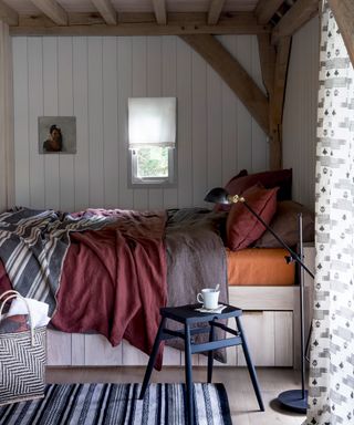 Luxury shed ideas featuring a built-in bed with red, blue and orange linen in a timbered shed.