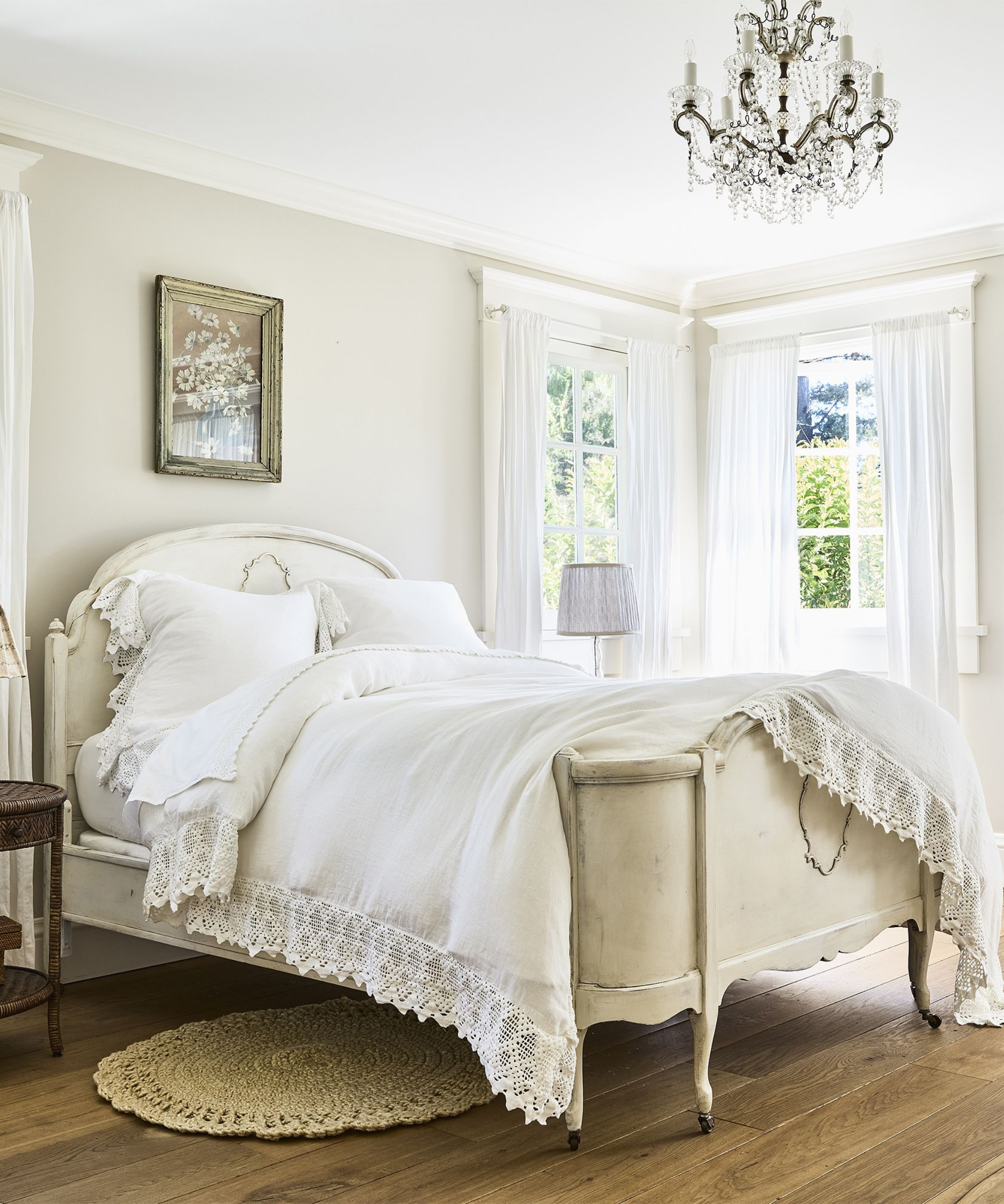a rustic bedroom with white painted walls, two windows in the corner, a white bed spread, and a small rug on the floor