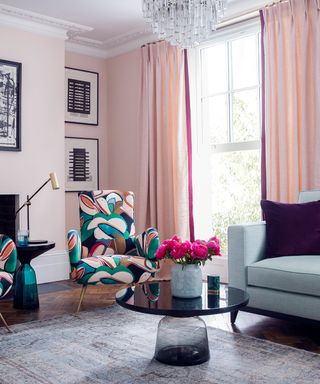 A pink living room with glass chandelier and abstract floral print chairs.