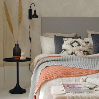 Double bed with grey headboard, grey, orange and cream bedding and throws, painted floorboard, natural rug and walls
