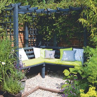 Wooden seating area with pergola in gravel patio area in garden surrounded by plants