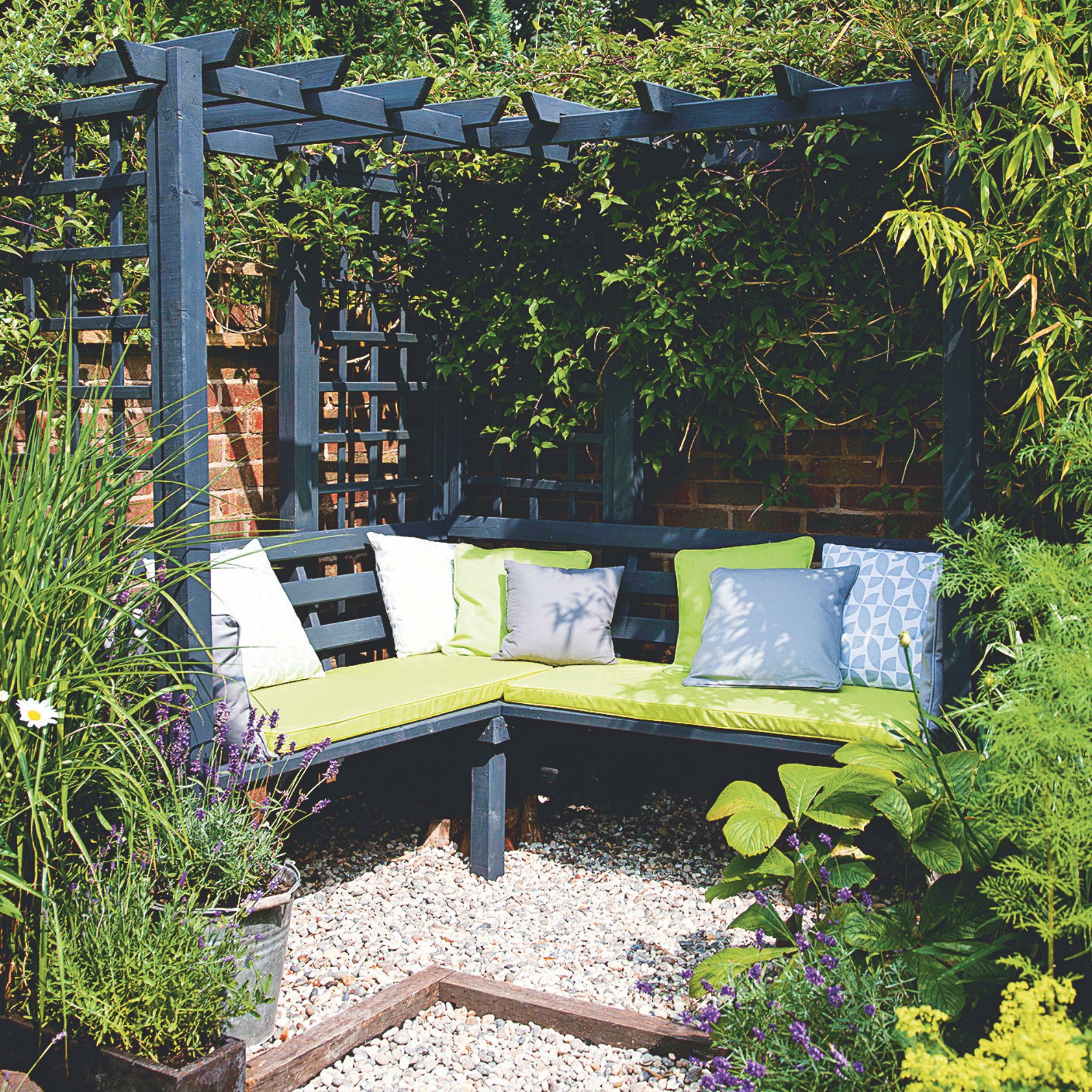 Wooden seating area with pergola in gravel patio area in garden surrounded by plants