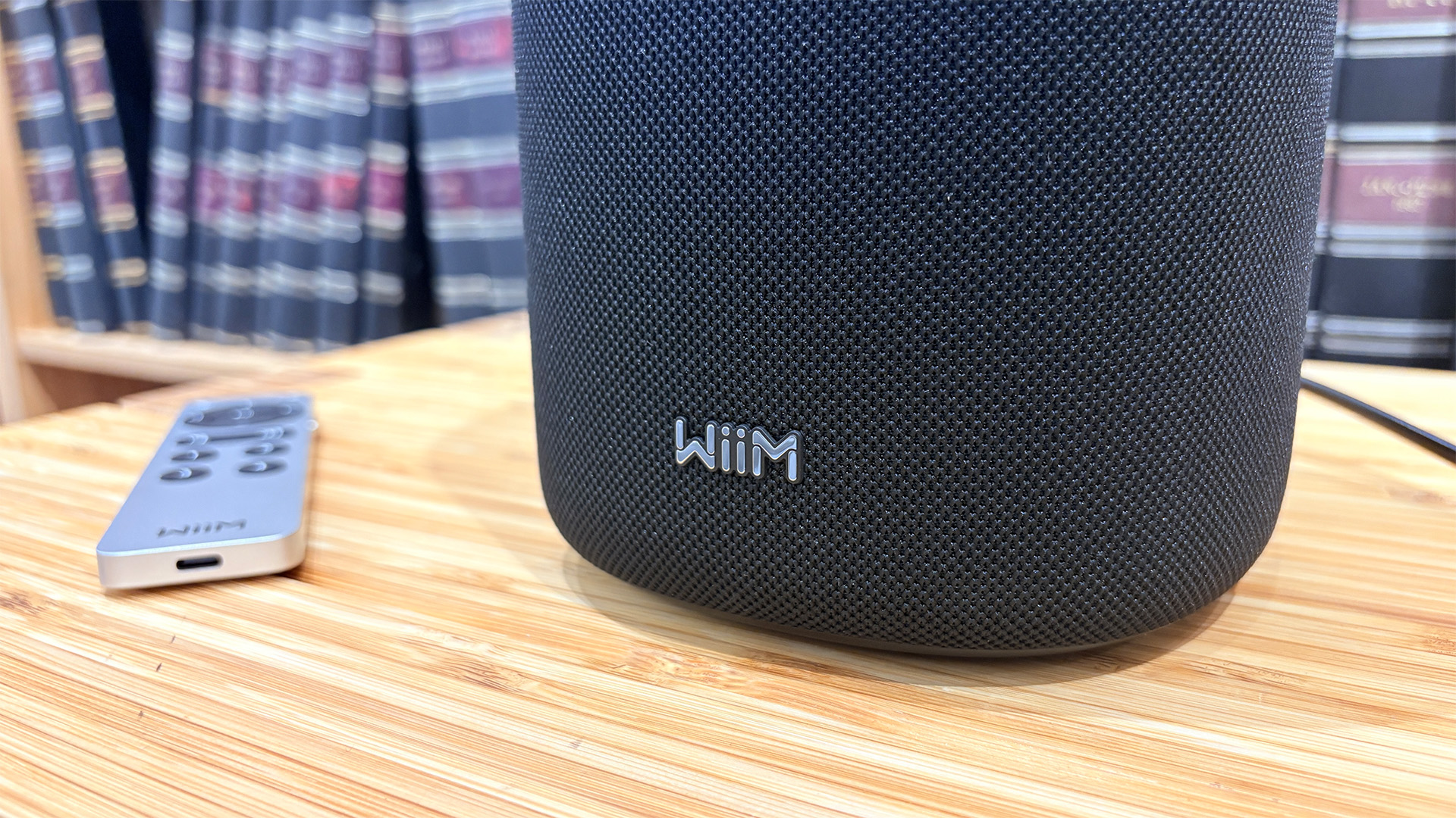 WiiM Sound wireless speaker next to remote on wooden hi-fi rack