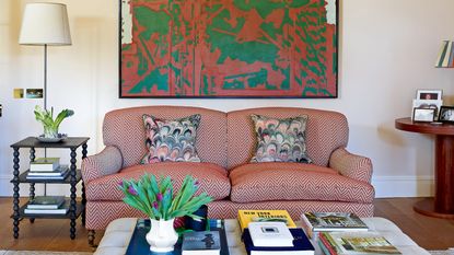  neutral living room with red zig zag sofa, pink and green artwork, and off white buttoned ottoman