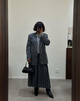 @frannfyne wearing a pleated grey skirt, blazer and boots