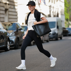 Diane Batoukina wears a black with embroidered NY logo pattern cap from New Era, a white with black faded logo print pattern t-shirt from Saint Laurent Paris, a black wool pullover knot at the shoulder, a black shiny leather large shoulder bag from Zadig&Voltaire, black legging pants, white socks, white leather and suede sneakers from Chanel, during a street style fashion photo session, on April 21, 2023 in Paris, France. 