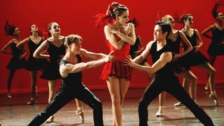 Amanda Schull wearing a red dress on stage while other dancers in black are around her in 'Center Stage'