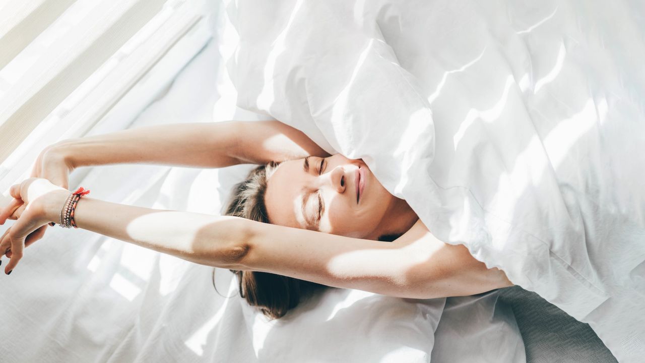 A woman stretches in bed while smiling