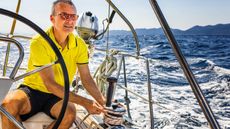 Older man behind wheel of sailboat and holding a rope