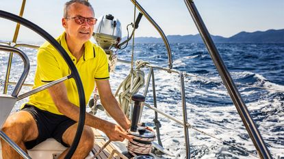 Older man behind wheel of sailboat and holding a rope