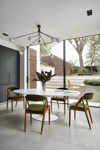 dining room with white table and green chairs, statement pendant light and sliding doors