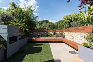 A modern urban garden with wooden built-in seating and a lawn