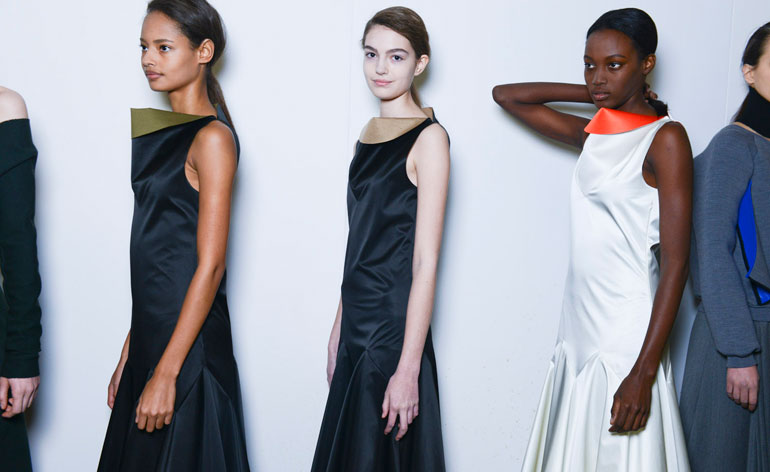Two women in dark blue silk dresses, and one in a white silk dress with an orange collar