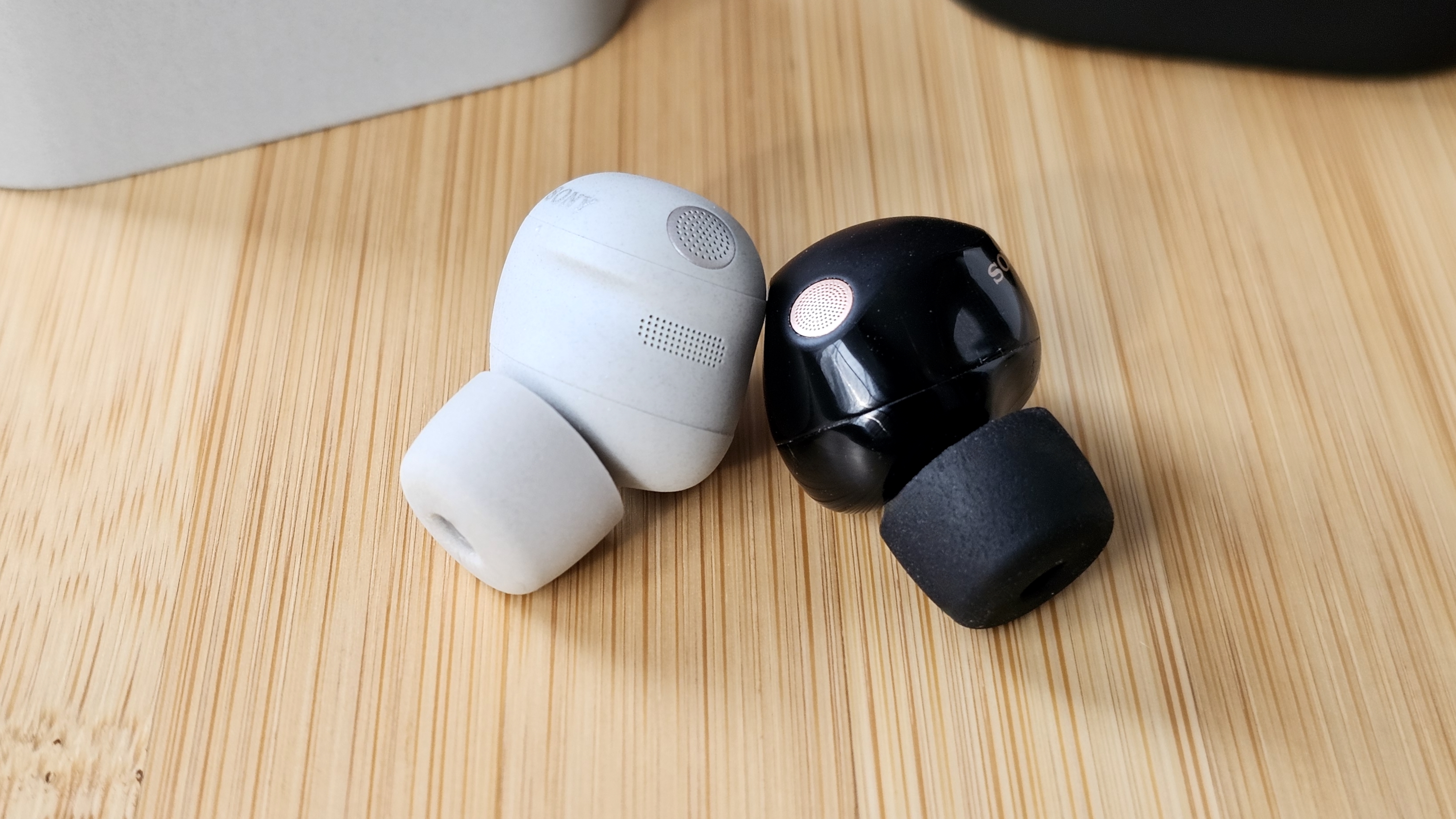 The Sony WF-1000XM6 and WF-1000XM5 side by side in a comparison, on a light wood table 