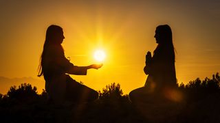 Two silhouetted individuals meditating opposite each other at sunset