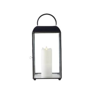 A black metal rectangular lantern with a white pillar candle in the middle of it and a curved black handle on top