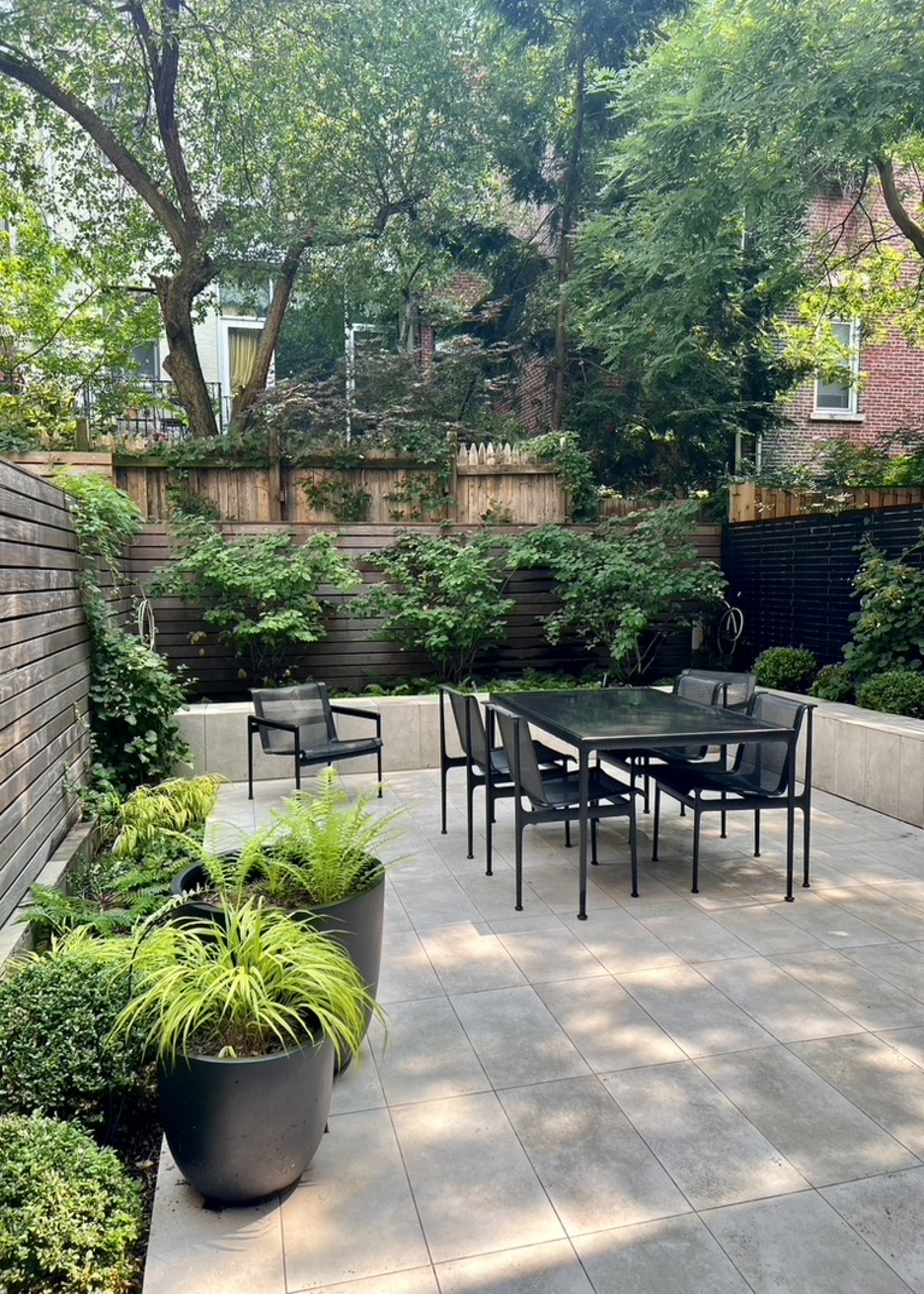A garden patio with a dining set and chairs, wooden slat fencing, and a border of green plants