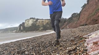 A man wearing Saxx Roast Master Mid-Weight Tights runs along a stony beach.