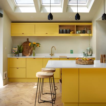 a modern yellow kitchen with white worktop and a breakfast bar with wooden stools