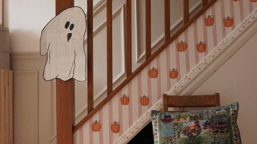 hallway stair rail with painted pumpkin and stripes on the panel and a cardboard ghost stuck on the newell post