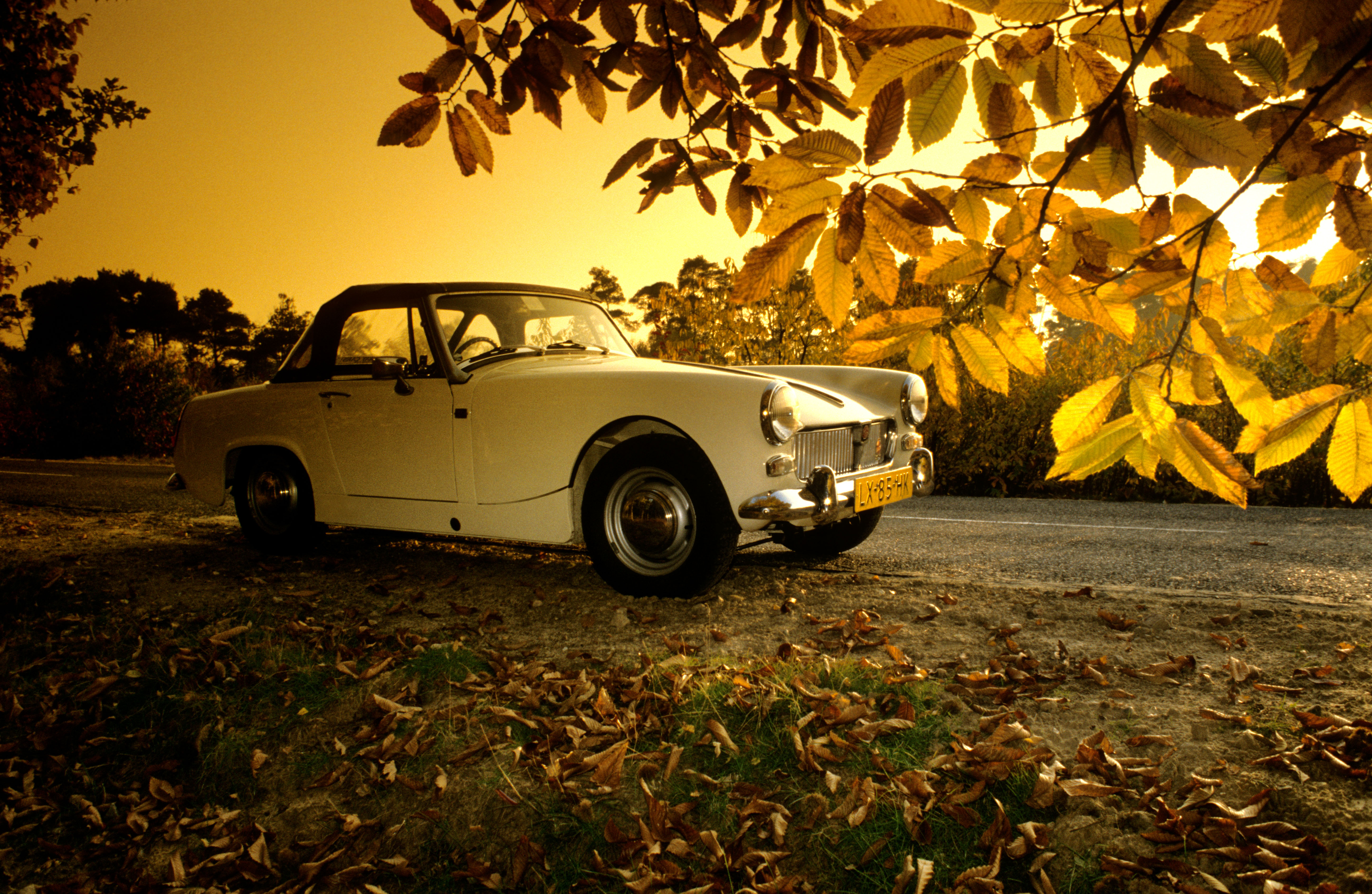 Stationary 1967 MG Midget on country road under evening sunlight