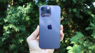 En blå iPhone 14 Pro Max holdes op af en hånd med bagsiden vendt mod kameraet.