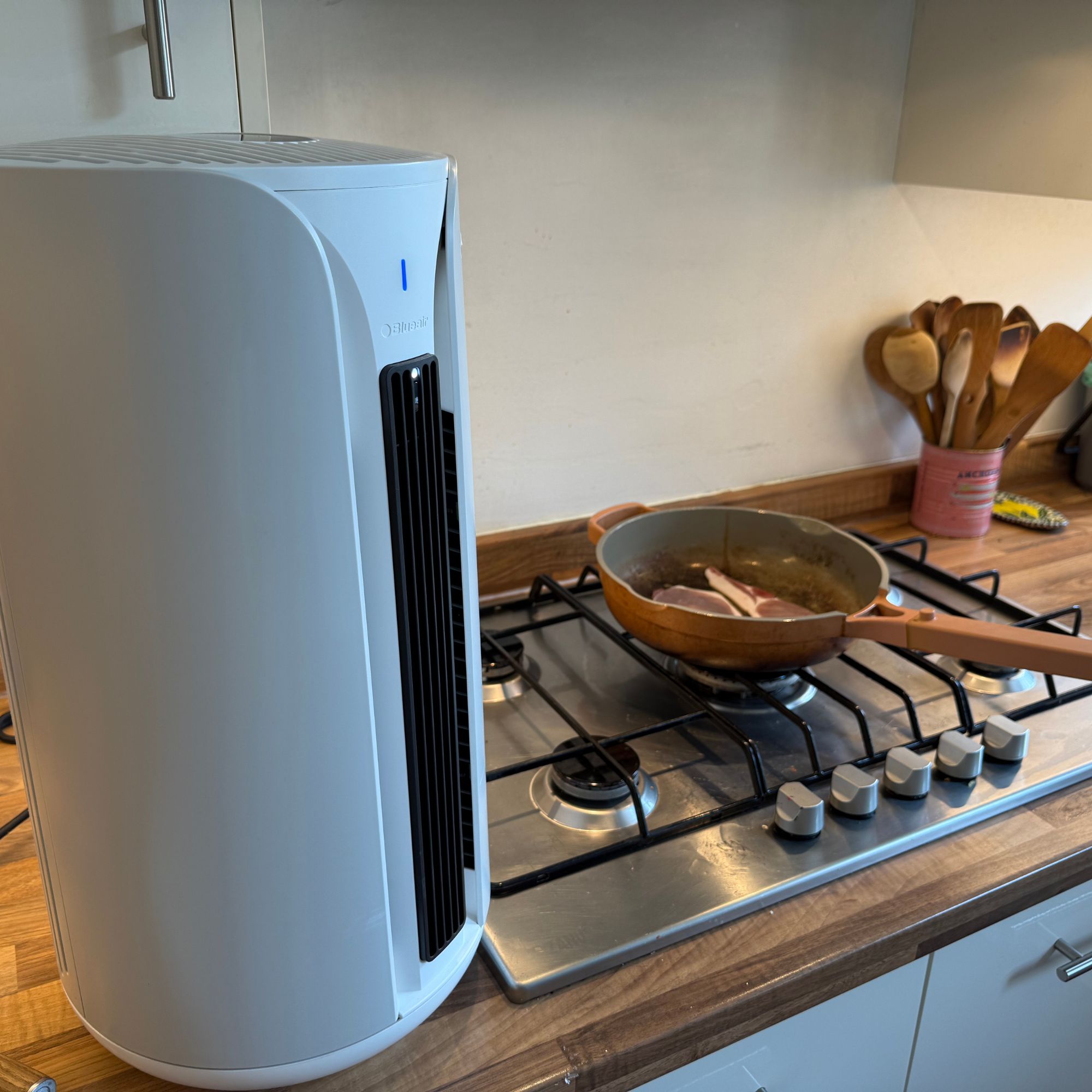 Blueair ComfortPure 3-in-1 T10i Air Purifier on a kitchen counter next to bacon frying in a pan
