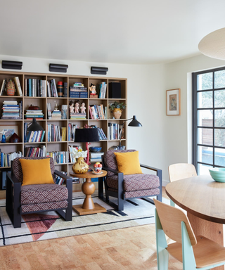 A white room with bright windows, two armchairs, a dining table and large bookshelves.