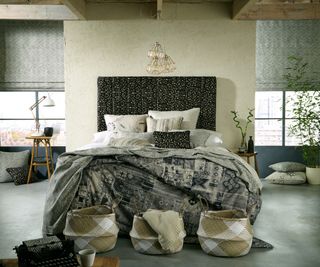 bedroom with woven baskets, variety of fabric finishes used on bed, wooden beams and large windows either side of bed
