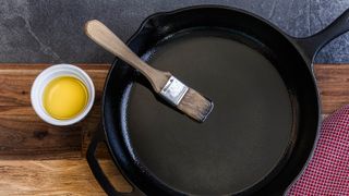 Oil being applied with a brush to a cast iron skillet