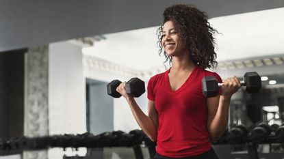African-american fitness woman doing biceps workouts with dumbbells in gym