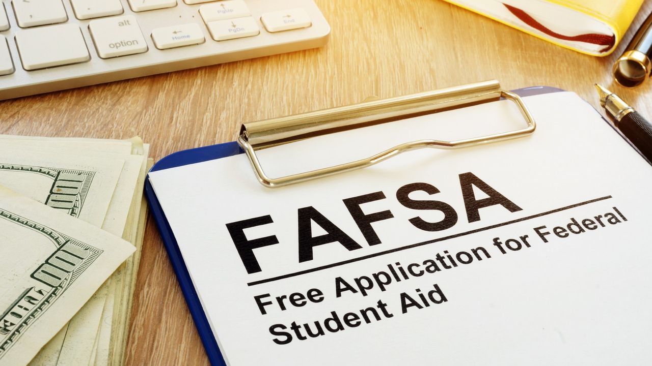 FAFSA form sitting on a desk with 100 dollar bills and a computer keyboard