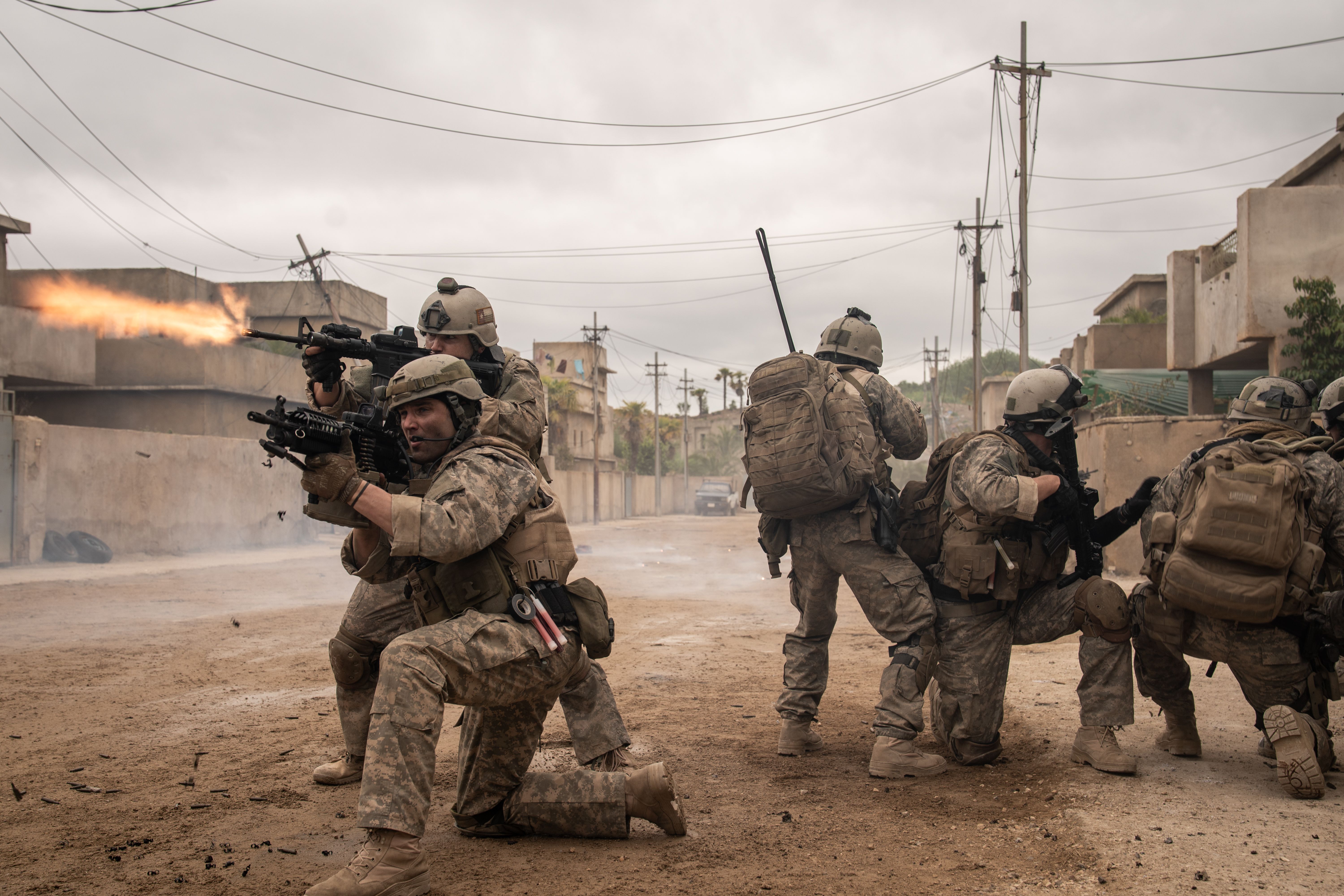 A group of soldiers in full gear firing on enemies, some are kneeling some are standing.