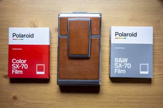 Polaroid SX70 camera folded away on table alongside color and monochrome packs of SX70 film