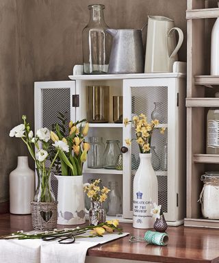 Countertop with flower arranging items and cupboard and shelves with vases