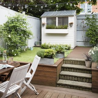 garden with decking and lawn areas and small white shed with a window box