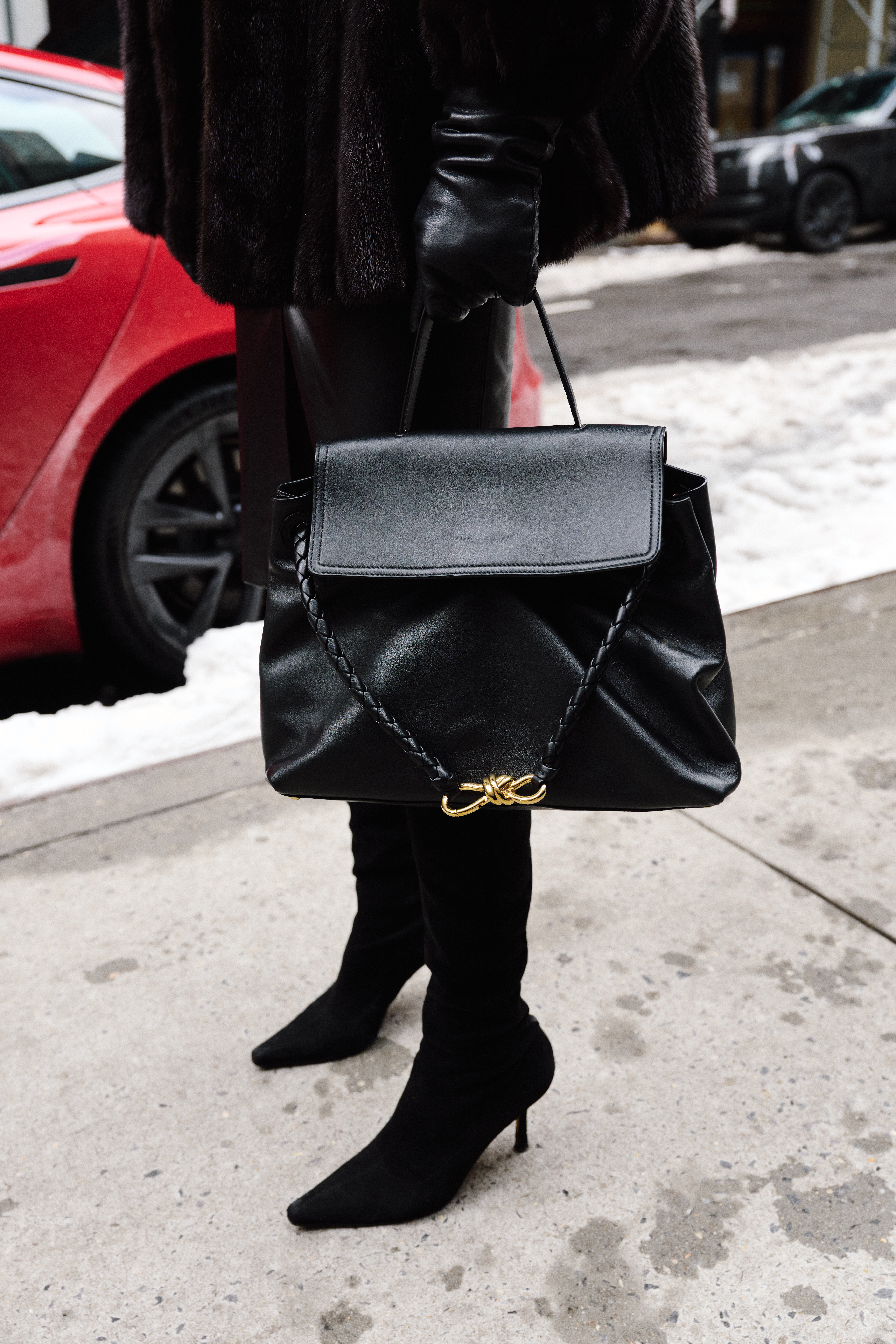 Eliza Huber wearing a brown fur coat, black leather jacket, black pencil skirt, black tights,  black suede boots, and black sunglasses while carrying a black Bottega Veneta Ciao Ciao bag outside of the Ulla Johnson show in Soho.