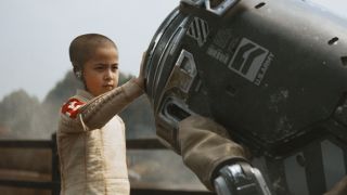 Still from the movie "The Creator." A young boy, who is actually a robot, has his hand on a piece of big machinery.