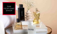 The Perfume Shop Logo placed over a selection of high end perfumes on a bedside table