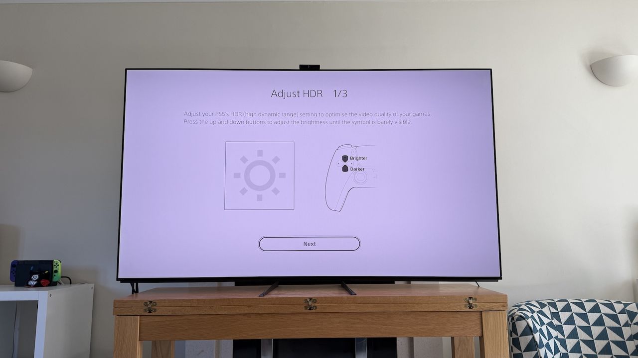 The 65-inch Sony A95L pictured on a wooden table in a living room. On the screen is the PS5 Adjust HDR menus