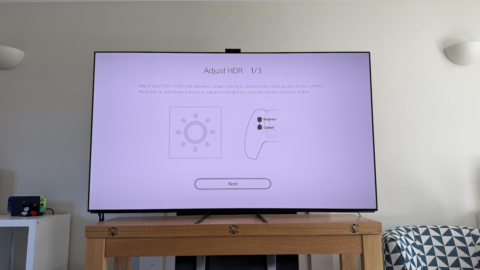 The 65-inch Sony A95L pictured on a wooden table in a living room. On the screen is the PS5 Adjust HDR menus