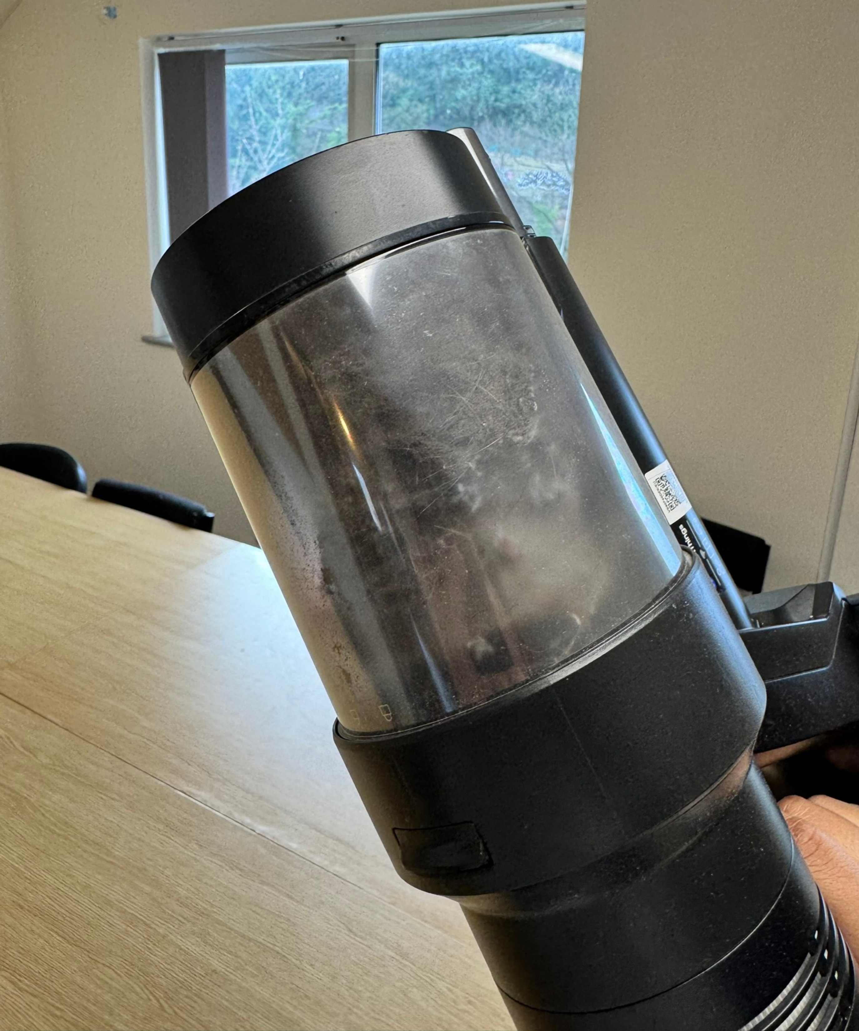 Samsung Bespoke AI Jet Ultra's dustbin filled with fur, held above wooden table and in front of window.