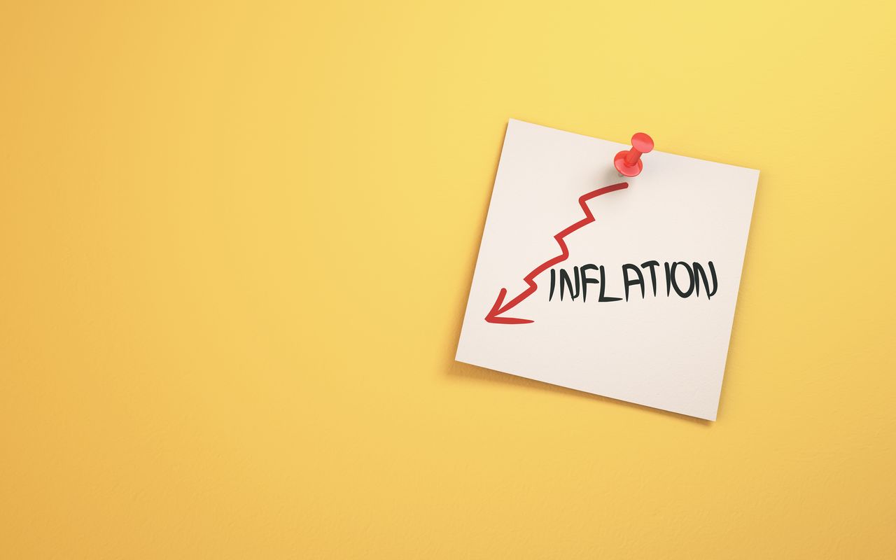 Post-It note that says &quot;inflation&quot; with red arrow pointing lower pinned to bright yellow backdrop